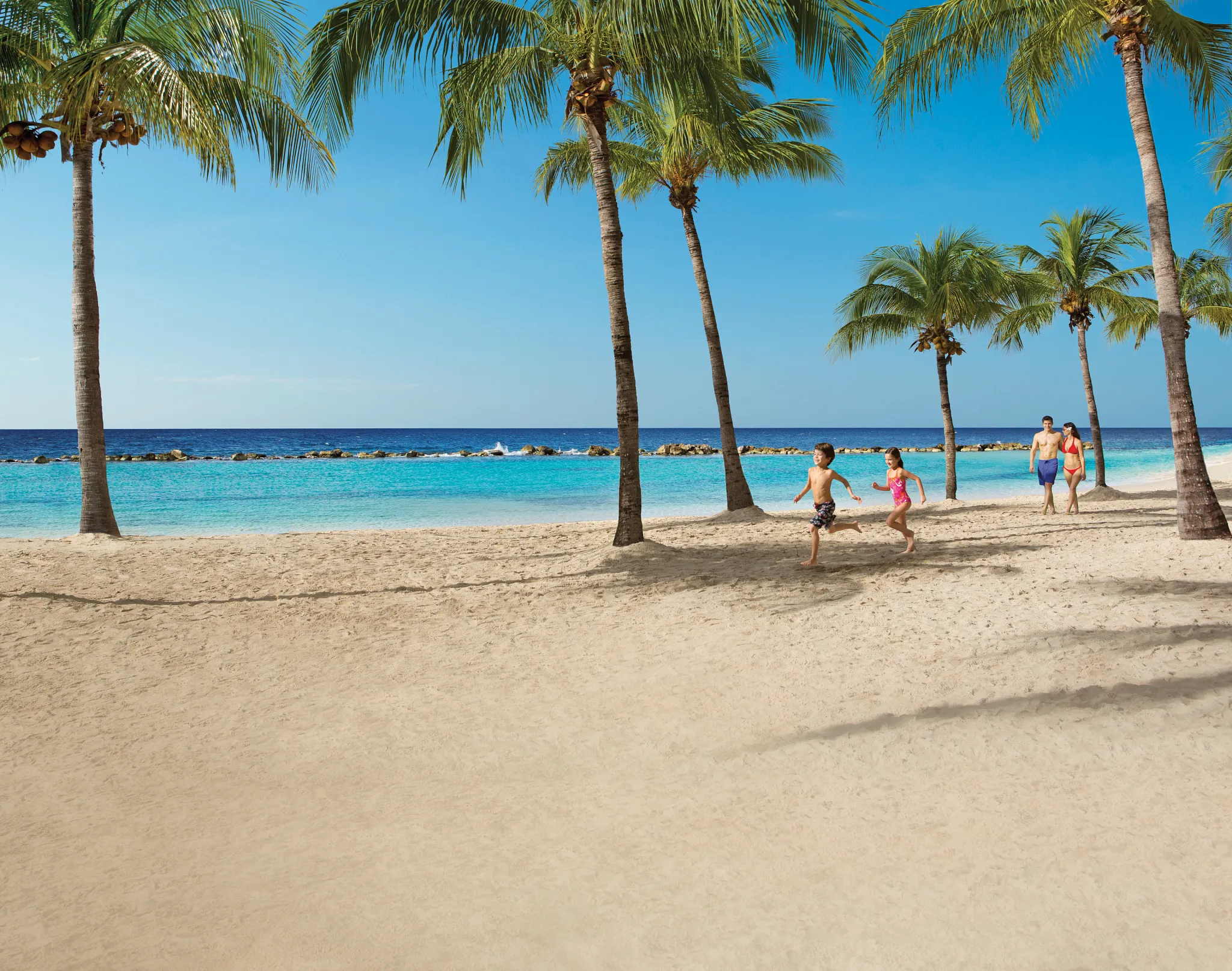 Family walking and children playing on the beach at Sunscape Curaçao Resort, Spa & Casino.
