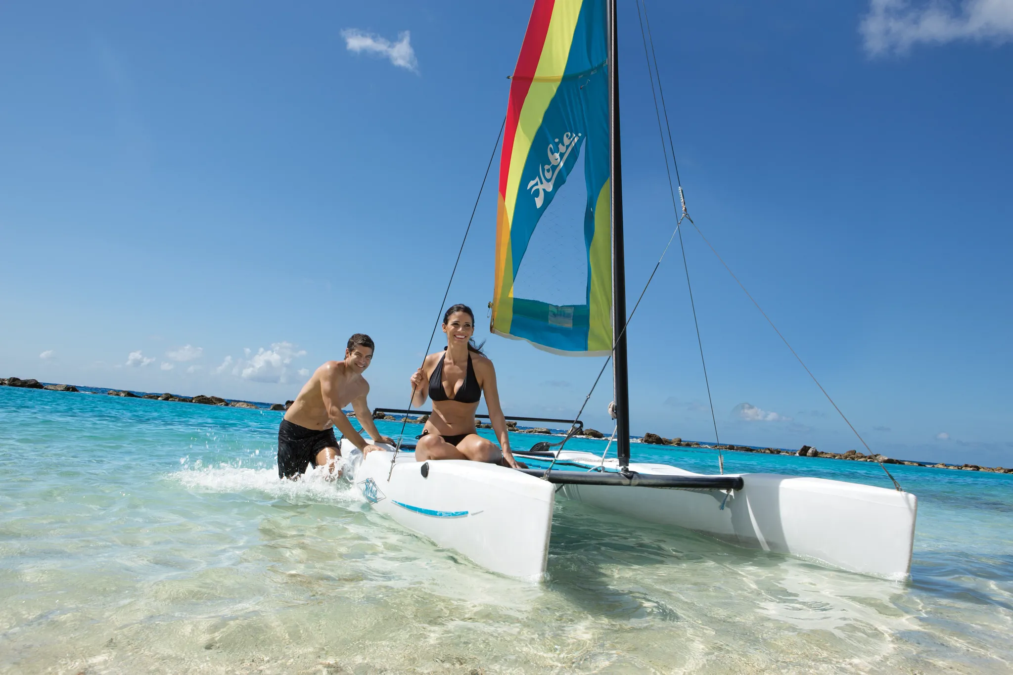Couple launching a Hobie Cat sailboat in the turquoise Caribbean waters at Sunscape Curaçao Resort, Spa & Casino.